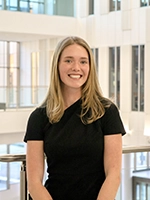 A smiling woman poses for a photo in a modern, bright building with large windows.