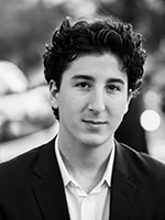 Black and white headshot of a young man with curly hair, wearing a suit jacket and white shirt.