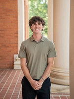 A young man smiles confidently while standing outdoors in front of columns and brick walls.