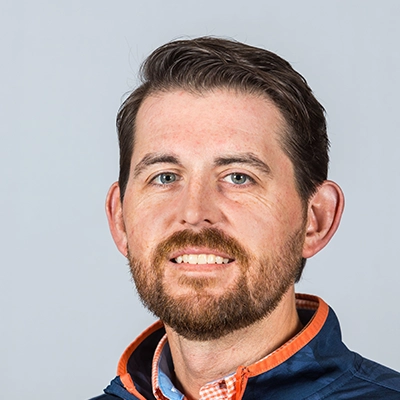 Headshot of a smiling man with a beard, wearing a navy jacket and a checked shirt.