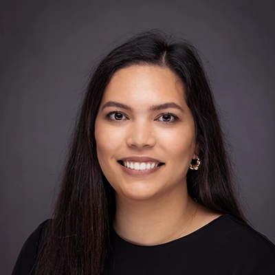 Professional headshot of a woman with long dark hair, wearing a black top and earrings, set against a dark background.