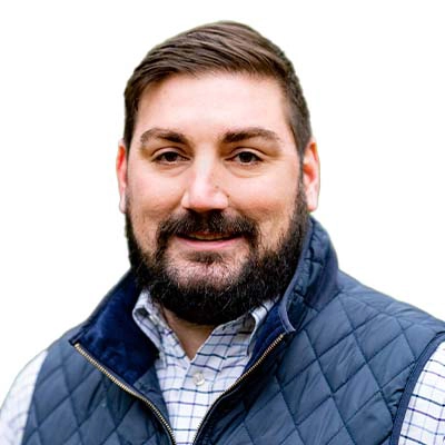 Headshot of a man with a beard wearing a navy blue vest and a checkered shirt.