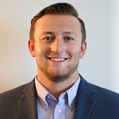 Professional headshot of a young man in a suit and collared shirt, smiling at the camera.