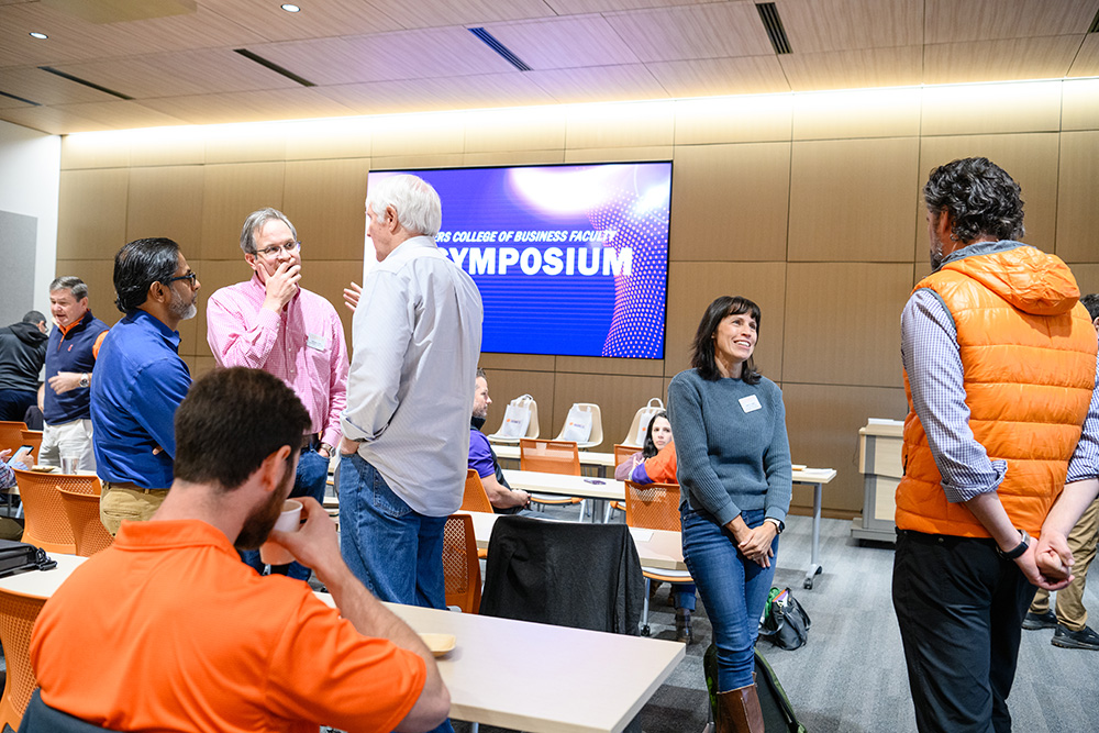 A group of professionals engages in conversation during a business faculty symposium. The event promotes networking and collaboration among educators and industry leaders.