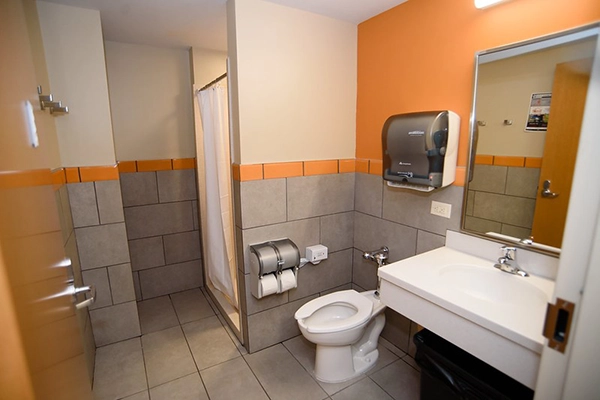 A clean and modern bathroom featuring a toilet, sink, and shower area, with gray tile and an orange accent wall.