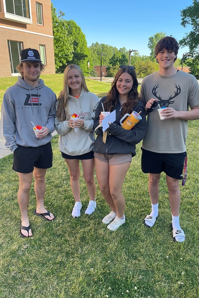 A group of four young adults enjoying frozen treats outdoors on a sunny day.