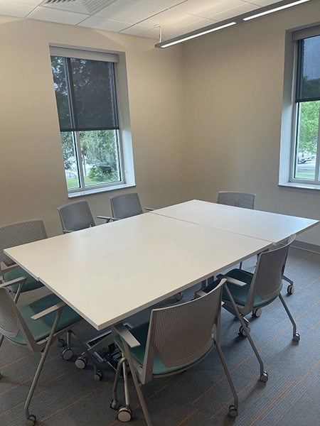 A modern conference room featuring a large white table surrounded by multiple rolling chairs and windows allowing natural light.