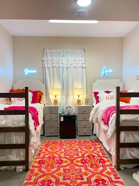 A brightly decorated shared bedroom featuring two twin beds with personalized neon lights and colorful bedding. A vibrant rug adds warmth to the space.