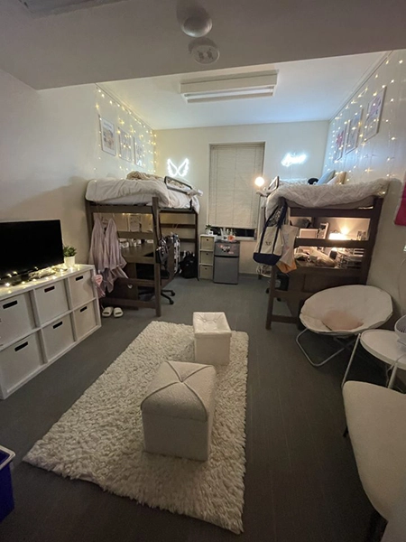 Cozy dorm room featuring two lofted beds, fairy lights, and a stylish rug, with a television and decorative elements creating a warm atmosphere.
