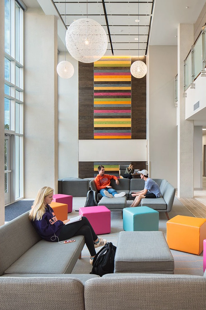 Modern lounge area featuring colorful seating cubes and a vibrant wall art installation, with students engaging in various activities.