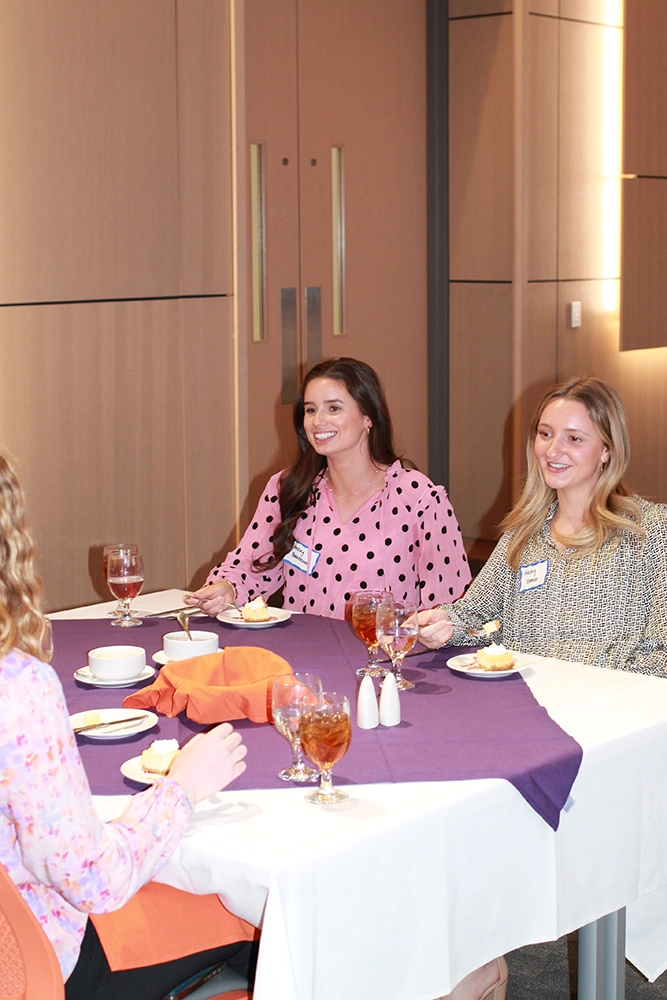 Two women are seated at a dining table, smiling and enjoying dessert during a gathering event.