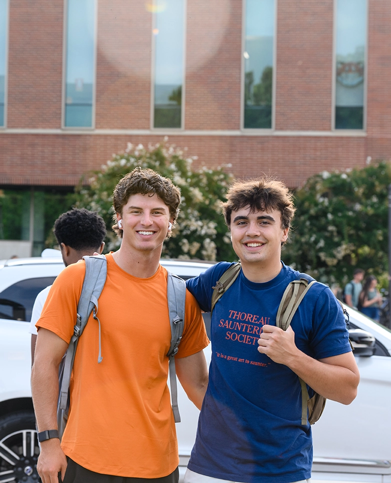Two college students smiling and posing for a photo outdoors on campus, with a modern building in the background.
