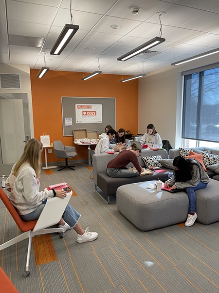 Group of students engaged in creative activities inside a modern lounge space with orange accents.