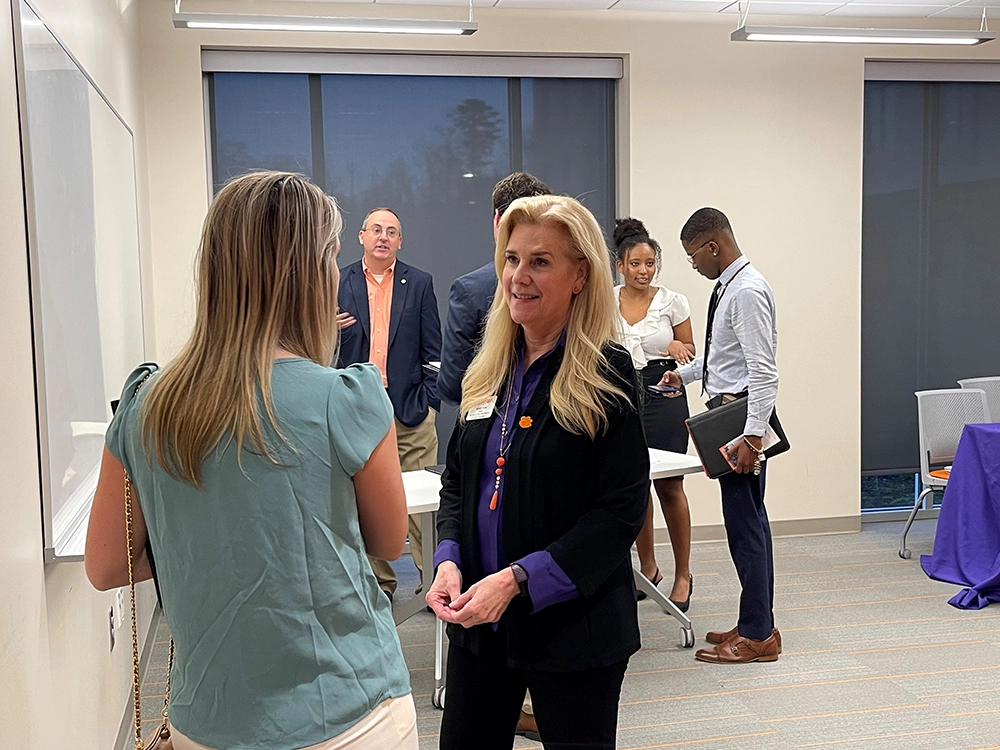 A professional networking event featuring a conversation between two women, with other attendees in the background.