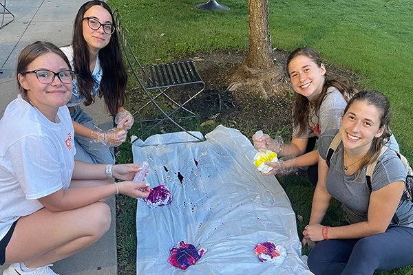 A group of four women enjoying a creative activity outdoors, preparing to dye fabric with vibrant colors.