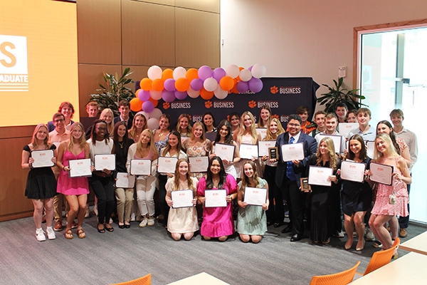 A group of students proudly holding certificates at a business honors event, surrounded by balloons and celebratory decorations.