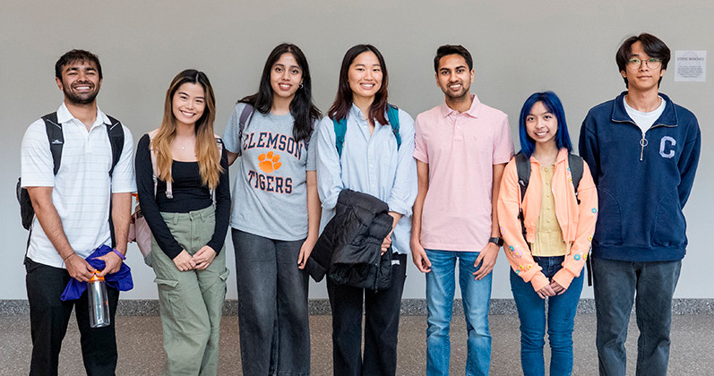 A group of diverse students standing together, smiling in a university hallway.