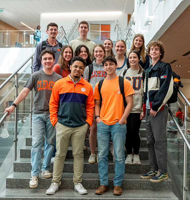 A group of students posing together on stairs, wearing Clemson University apparel.