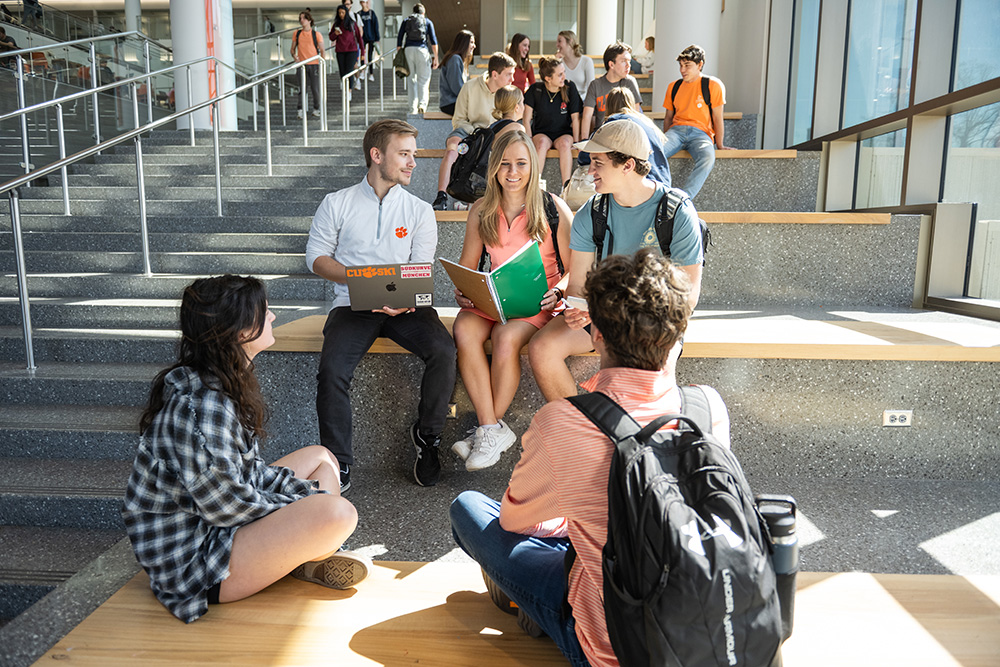 A group of college students engaging in collaborative study on campus stairs, with laptops and notebooks.