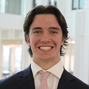 A young man in a suit and tie smiling confidently in a modern office environment.