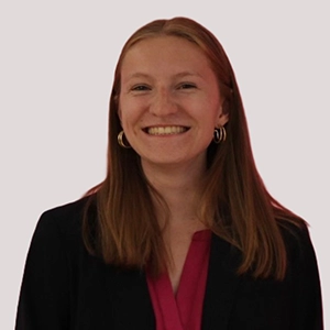 A smiling woman with long hair wearing a black blazer and pink top.