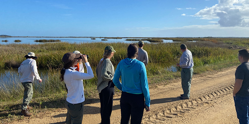 students on a dirt road looking at a marsh