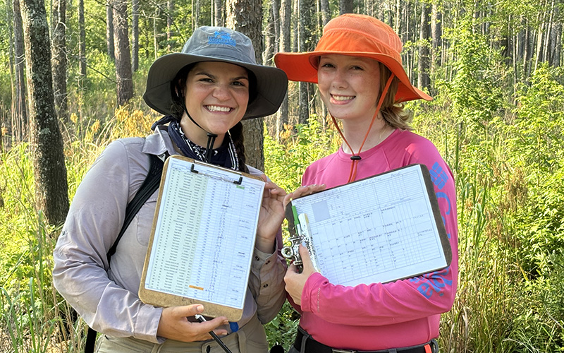 2 students with clipboards standing in a forest