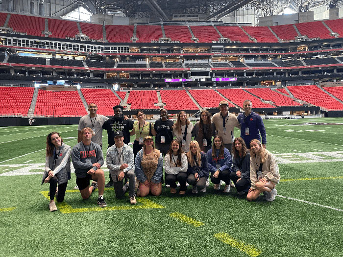Group of individuals posing on the football field inside a stadium, showcasing an event or outing.