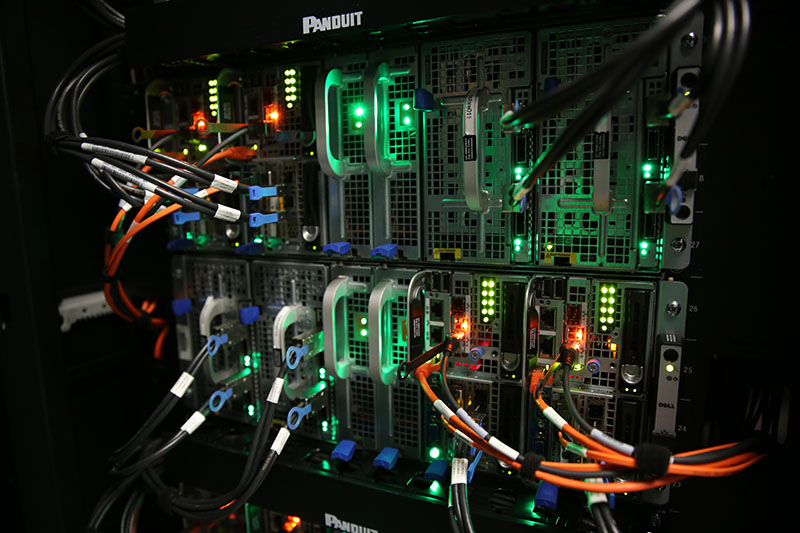 Close-up of a server rack with illuminated LED indicators and connected cables, showcasing a network infrastructure.