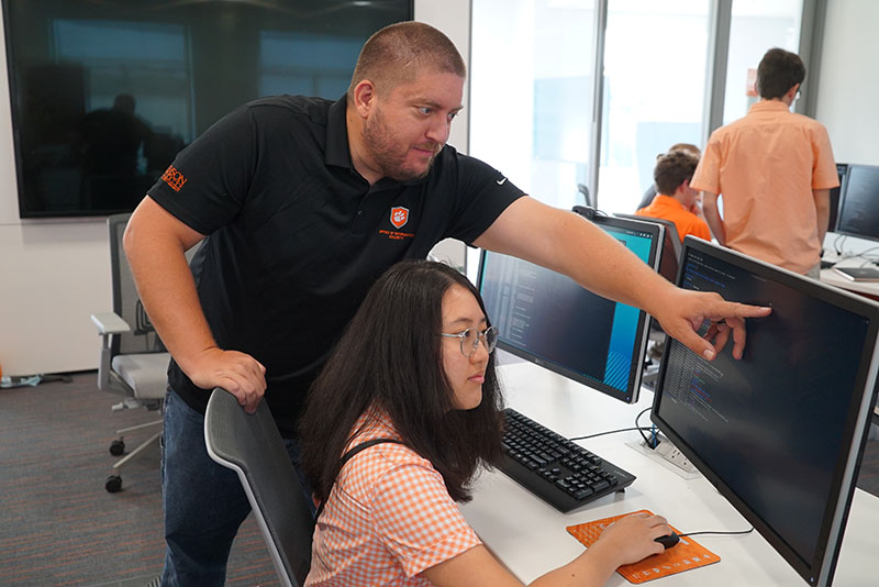 A Security Operations Center employee showing someone sitting at a computer something on the screen.