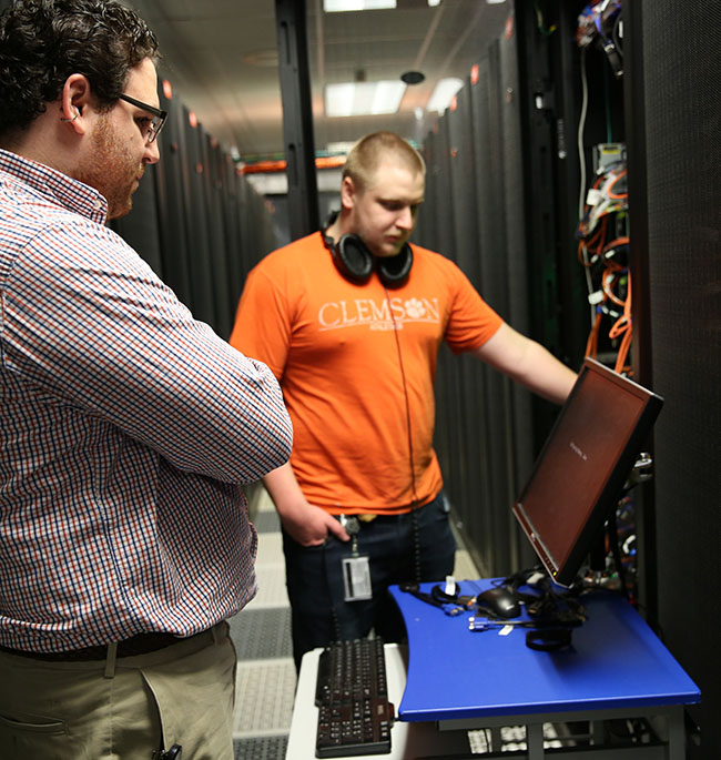 RCD staff collaborating in a server room, one observing while the other interacts with a computer monitor.