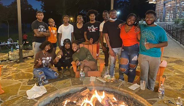 A group of Emerging Scholars students are gathered around a fire pit just after sun down.