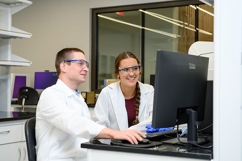 Two people working in lab, smiling, while looking at data on computer.