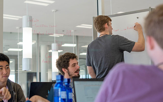 Students in Watt writing on whiteboard snd glass walls