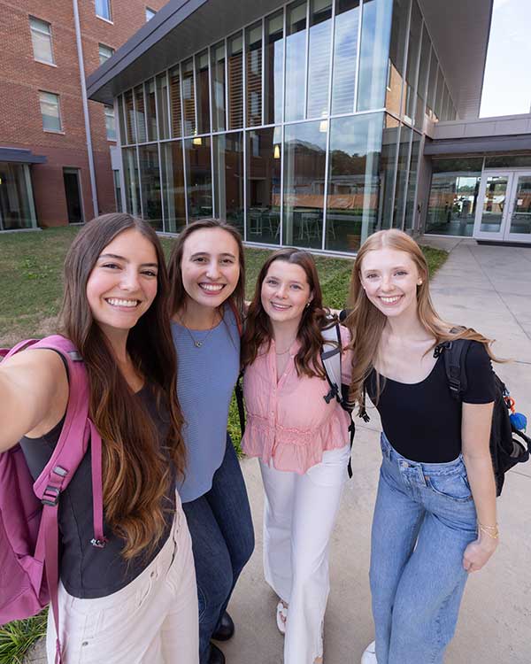 A group of four female Honors students posing for a selfie and smiling in front of the Honors Center.