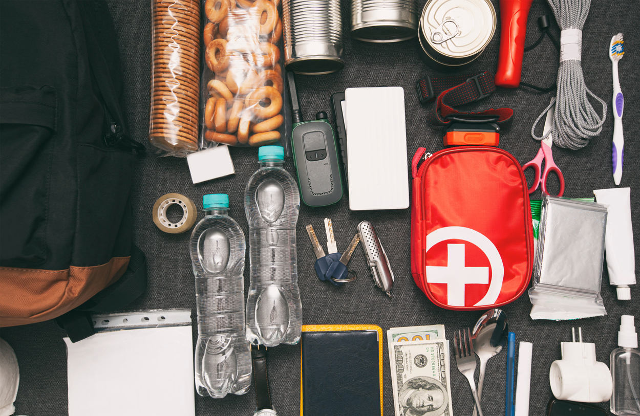 A collection of items to go in an emergency kit lined up on a gray couch.