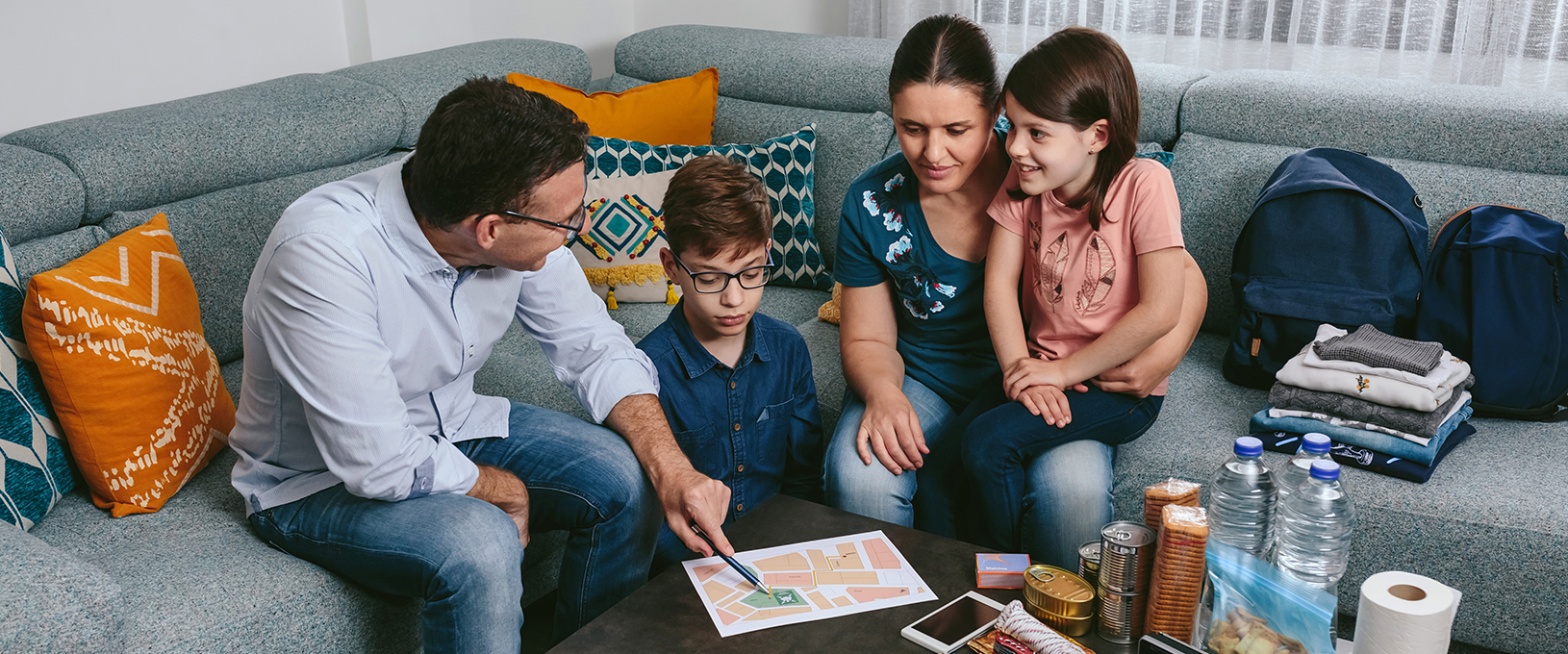 A family of four discusses their emergency plan in their living room, while building an emergency kit with necessary supplies.