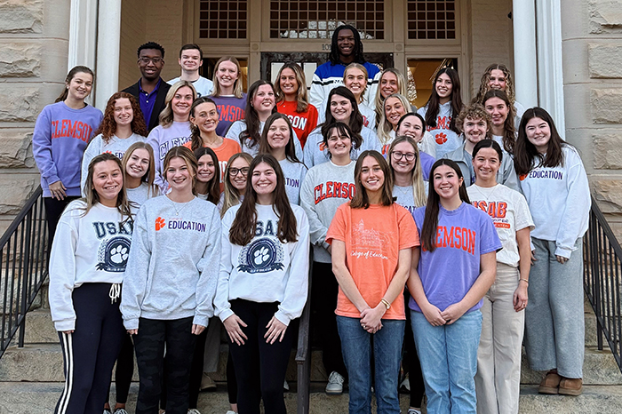 Group photo of college students in Clemson apparel, posing on the steps of a building.