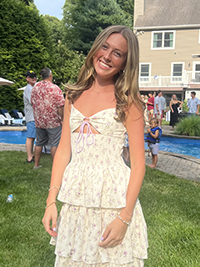 A young woman smiles while wearing a floral dress at a summer gathering by a pool.