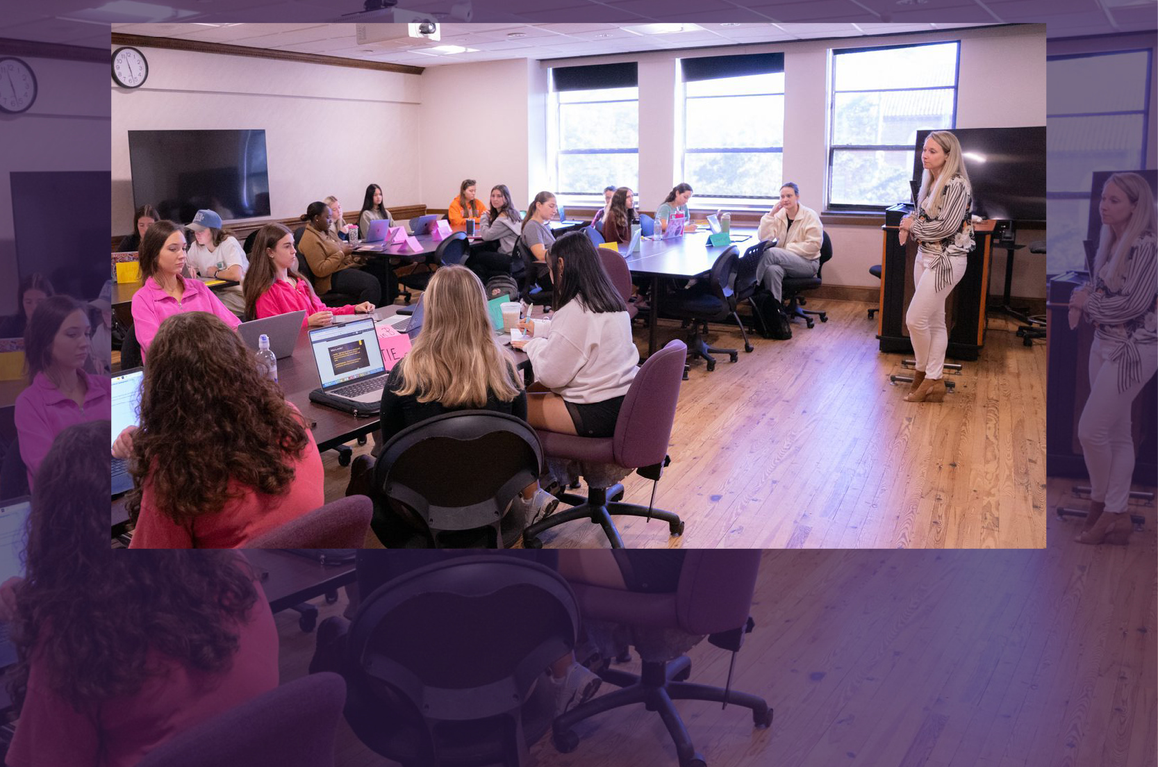 A classroom with undergraduates at tables, listening to the instructor in the front of the room.