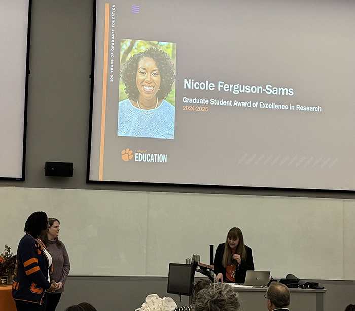 Woman receiving award with presentation with her name and photo above head.