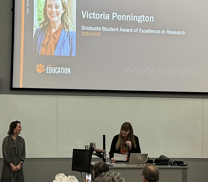 Woman receiving award with presentation with her name and photo above head.