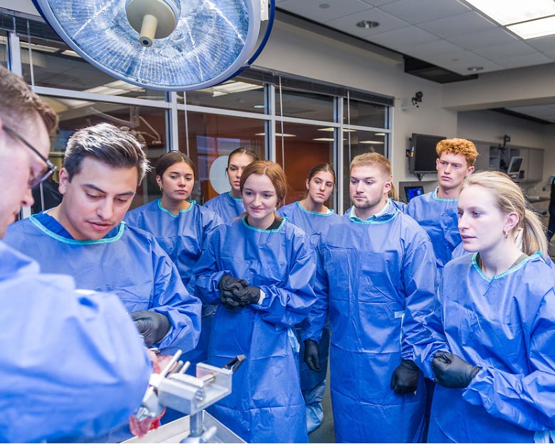 a group of students in blue surgical gowns observe a demonstration at Arthrex