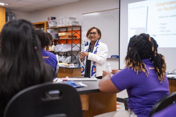 A female official speaks to a group of students in a classroom.