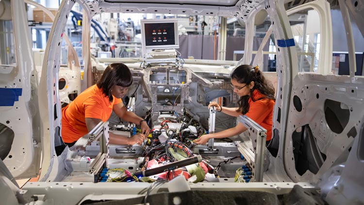 two female students at CU-ICAR Examine a test vehicle in a lab 