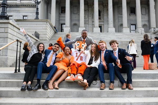 The Tiger Cub and Clemson students sit on the steps of the state capitol.