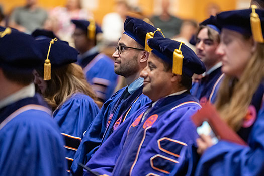 Smiling students look towards the stage at their doctoral commencement.