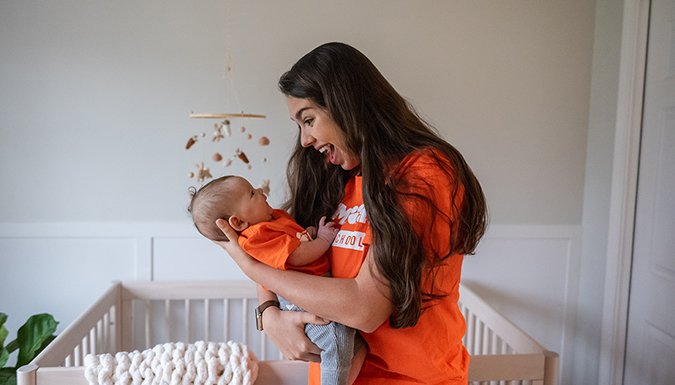 A mother holding her child, both wearing Clemson University attire.