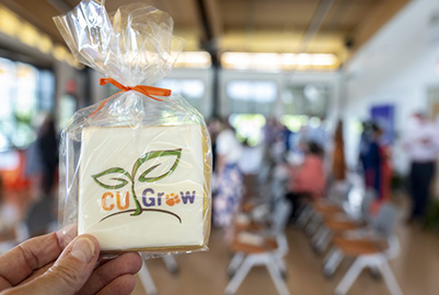 A hand holds a white cookie with the CU Grow logo printed on it.