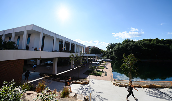 Students walk underneath Library Bridge with the Reflection Pond on the left.